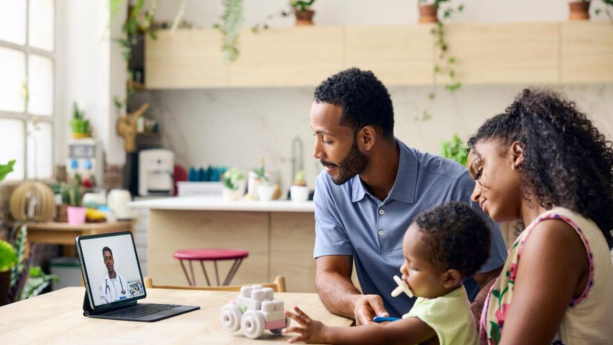 Parents and their toddler on a telehealth visit at their kitchen table